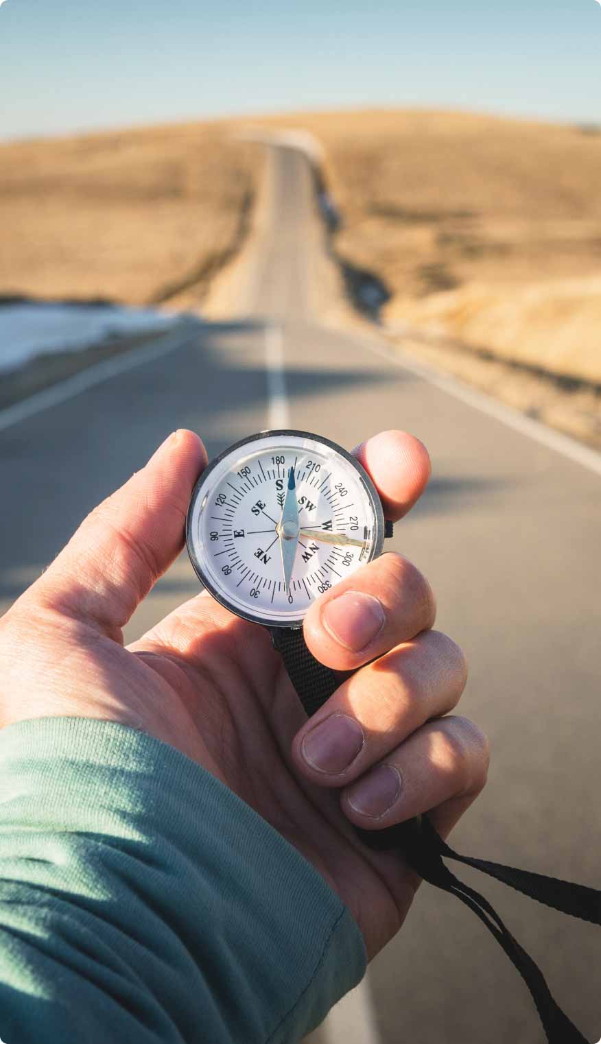 Woman's hand holding compass looking down a long road