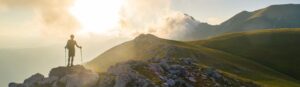 Hiker standing on rocks looking out on a mountain range at dawn